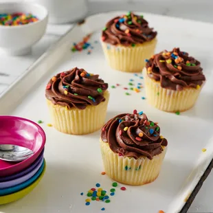 four cupcakes with chocolate frosting and sprinkles