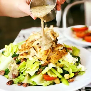 a person pouring dressing on a salad