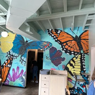 a woman sitting at a table in front of a mural of butterflies