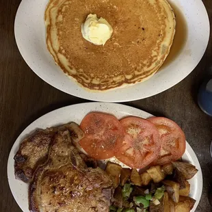 Jalapeño pork chops, home fries, tomatoes slices and pancakes with butter.