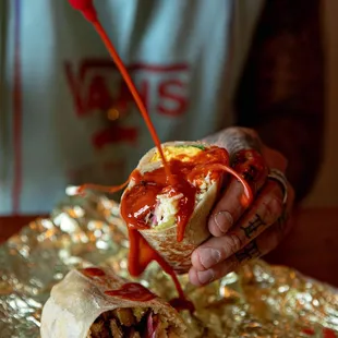 a person pouring ketchup on a burrito