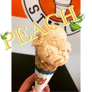 a hand holding a cone of peach ice cream