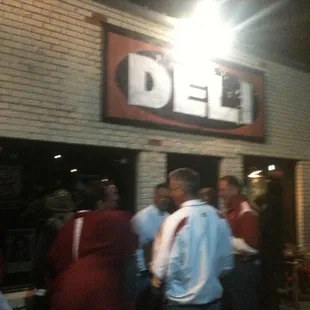 a group of people standing outside of a deli