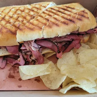 Pastrami sandwich on french bread with chips