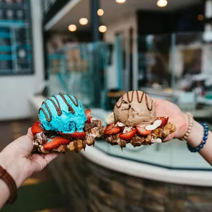 a hand holding a chocolate covered strawberry and ice cream sandwich