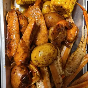 a tray of crab legs, potatoes, corn, and corn on the cob