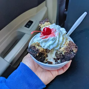 a hand holding a bowl of ice cream with a cherry on top