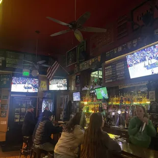 people sitting at a bar watching televisions