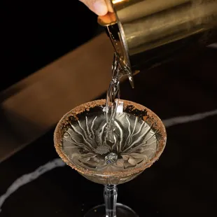 a person pouring a cocktail into a glass