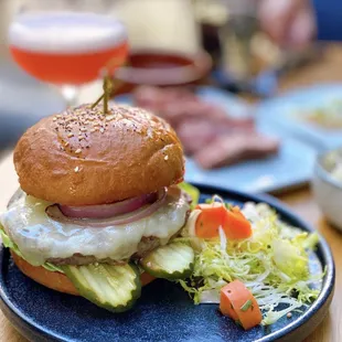 Wagyu Cheeseburger w/ cheddar, bibb, red onion, aoili, tomato, pickles | $18 (Background: Jimbo&apos;s Sour-$14)