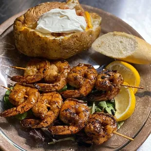 a plate of shrimp skewers and a baked potato