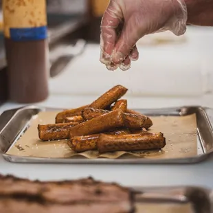 a hand sprinkling salt over a tray of hot dogs