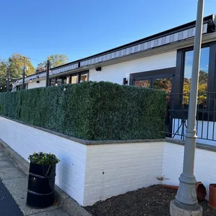 a white brick building with a green hedge in front of it