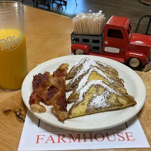 a plate of french toast, bacon, and a glass of orange juice