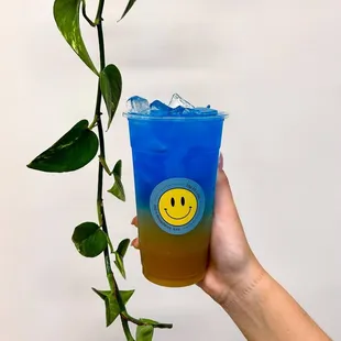 a hand holding a blue drink with a smiley face on it