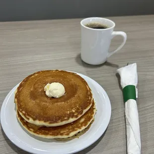 a stack of pancakes with butter and a cup of coffee