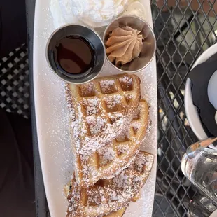 a plate of waffles with whipped cream and syrup