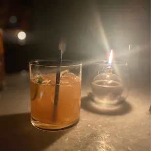 a drink in a glass with a straw and a candle in the background