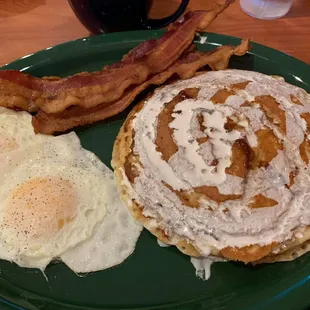 Cinnamon roll pancake platter with eggs over easy and bacon.
