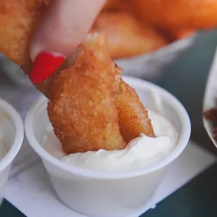 a person dipping a fried item into a bowl of dip