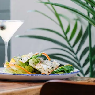 a plate of salad with a martini in the background