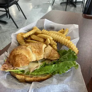 Ham and cheese on a croissant with fries.