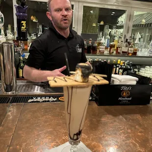 a man standing behind a bar with a chocolate milkshake