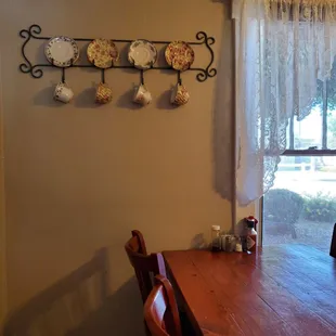 Cute collections of tea cups and plates on display, lace curtains, quaint wood tables and chairs