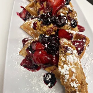 a plate of waffles topped with berries and powdered sugar