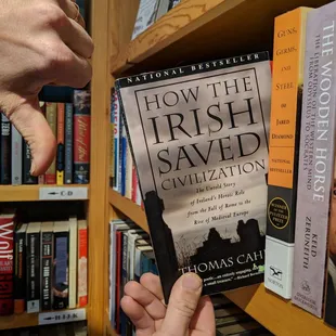 a person holding a book in front of a bookshelf