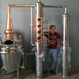 a man standing in front of a large copper still