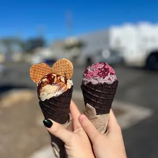 a person holding two waffle cones
