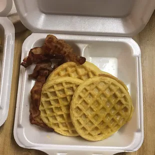 two waffles and bacon in a styrofoam container