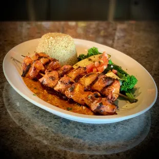 a plate of chicken skewers with rice and broccoli