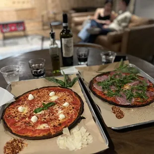 two pizzas on trays on a table