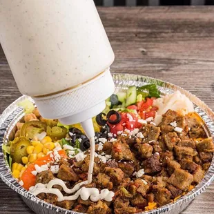 a person pouring dressing on a bowl of food