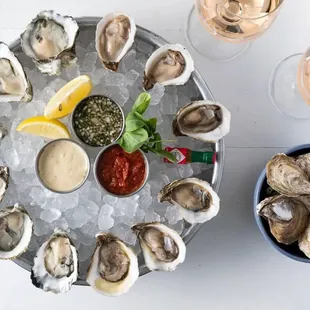 a platter of oysters with dipping sauce and lemon wedges