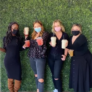 four women with face masks holding drinks