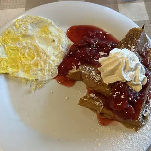 Half of an order of French toast topped with strawberries and whipped cream and a hard fried egg.