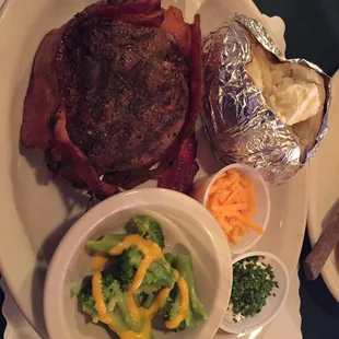 Venison wrapped in bacon accompanied by a baked potato and broccoli