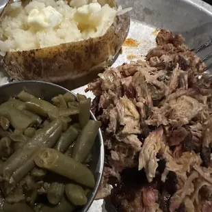 a plate of pulled pork, green beans, and a baked potato