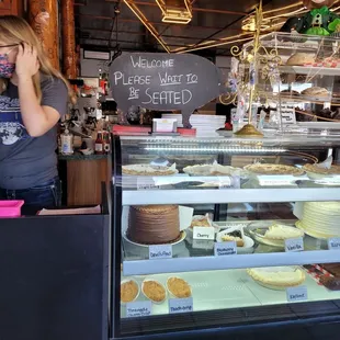 a woman standing behind a display case of baked goods