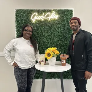 a man and a woman standing next to a table with a vase of sunflowers