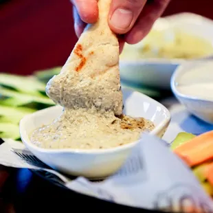a person dipping a pita into a bowl of dip