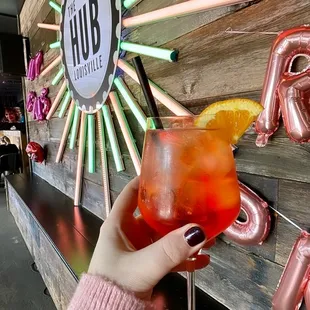 a person holding a cocktail in front of a neon sign