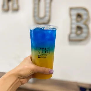 a hand holding a blue and yellow drink