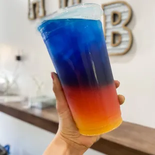 a hand holding a blue and red drink