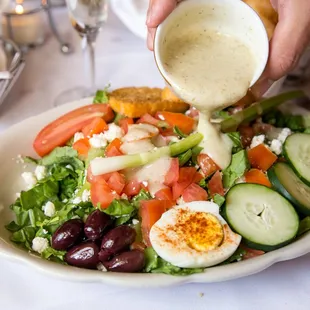 a person pouring dressing on a salad