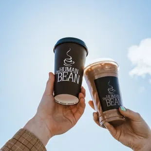 two hands holding two cups of coffee