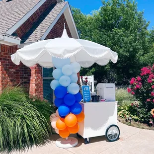 an ice cream cart with balloons and an umbrella